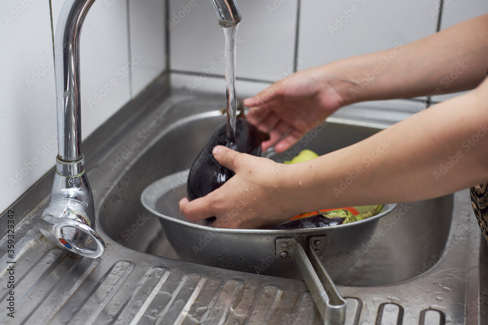 Cleaning organic eggplant in the kitchen. A woman washing freshly-picked ripe eggplant vegetable in colander