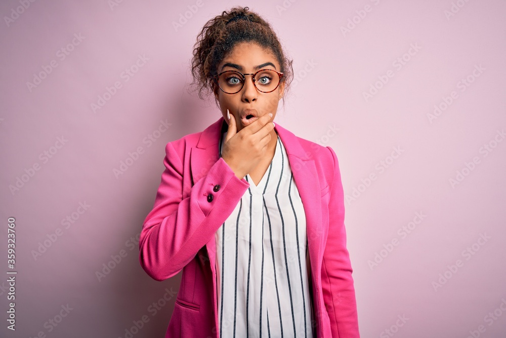 Beautiful african american businesswoman wearing jacket and glasses over pink background Looking fascinated with disbelief, surprise and amazed expression with hands on chin Beautiful african american businesswoman wearing jacket and glasses over pink background Looking fascinated with disbelief, surprise and amazed expression with hands on chin