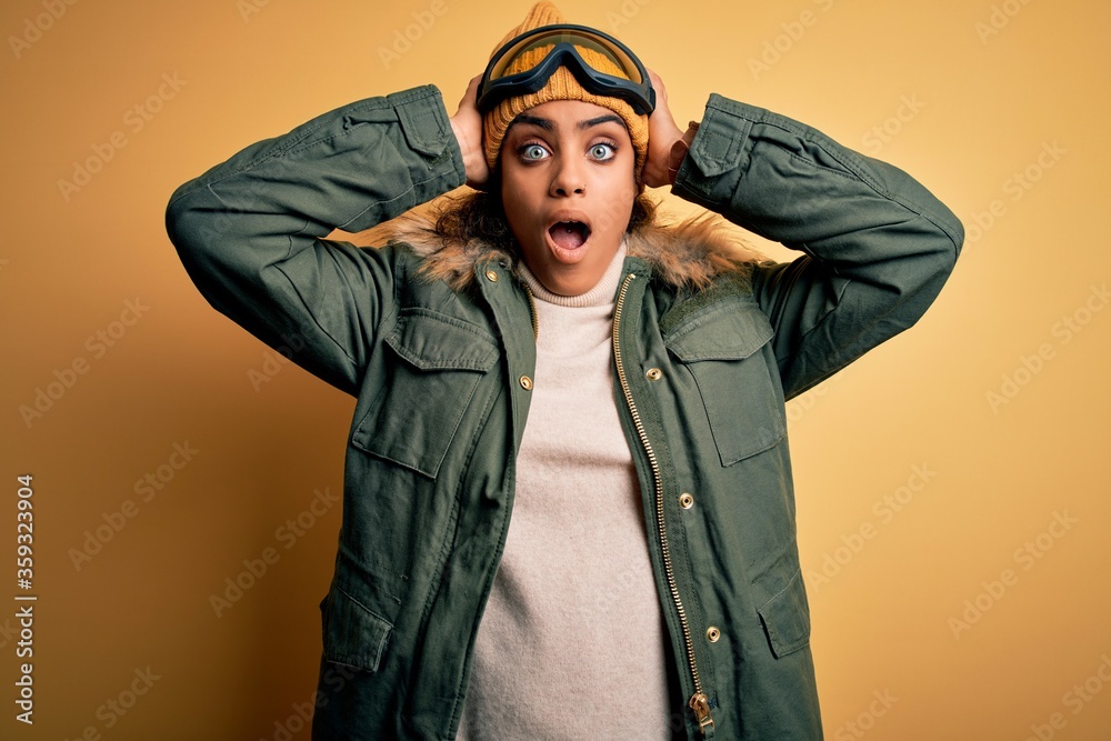 Young african american afro skier girl wearing snow sportswear and ski goggles Crazy and scared with hands on head, afraid and surprised of shock with open mouth Young african american afro skier girl wearing snow sportswear and ski goggles Crazy and scared with hands on head, afraid and surprised of shock with open mouth