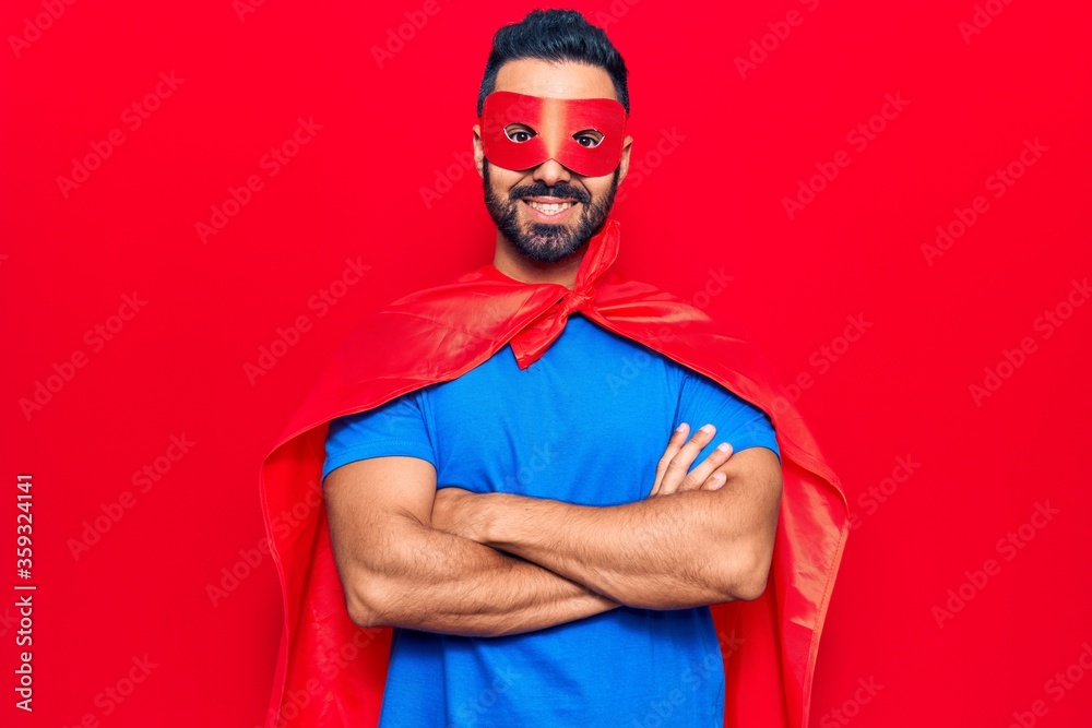 Young hispanic man wearing super hero costume happy face smiling with crossed arms looking at the camera. positive person.