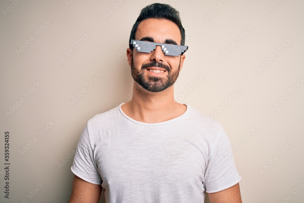 Young handsome man with beard wearing funny thug life sunglasses over white background with a happy and cool smile on face. Lucky person. Young handsome man with beard wearing funny thug life sunglasses over white background with a happy and cool smile on face. Lucky person.