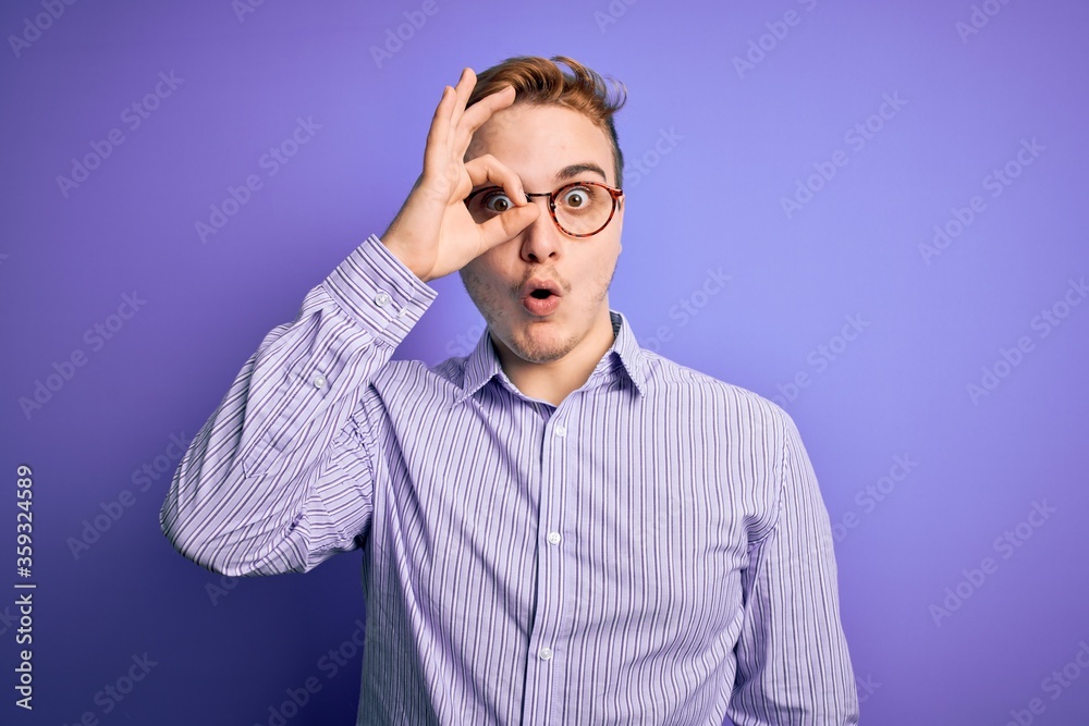 Fototapeta premium Young handsome redhead man wearing casual shirt and glasses over purple background doing ok gesture shocked with surprised face, eye looking through fingers. Unbelieving expression.