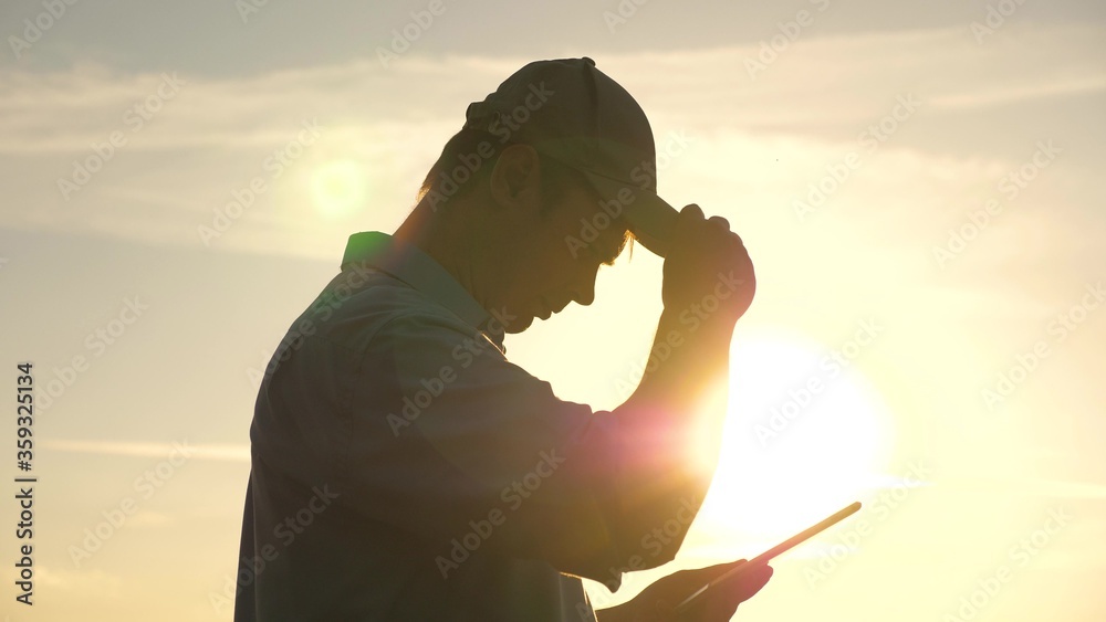 Farmer works with tablet on a wheat field in sun. silhouette of an agronomist with tablet studying wheat crop in the field. business man plans his income in the field. grain harvest.
