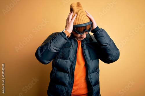 Young handsome skier man skiing wearing snow sportswear using ski goggles suffering from headache desperate and stressed because pain and migraine. Hands on head.