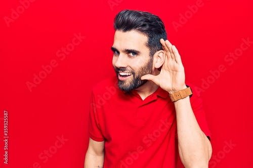 Young handsome man with beard wearing casual polo smiling with hand over ear listening and hearing to rumor or gossip. deafness concept.