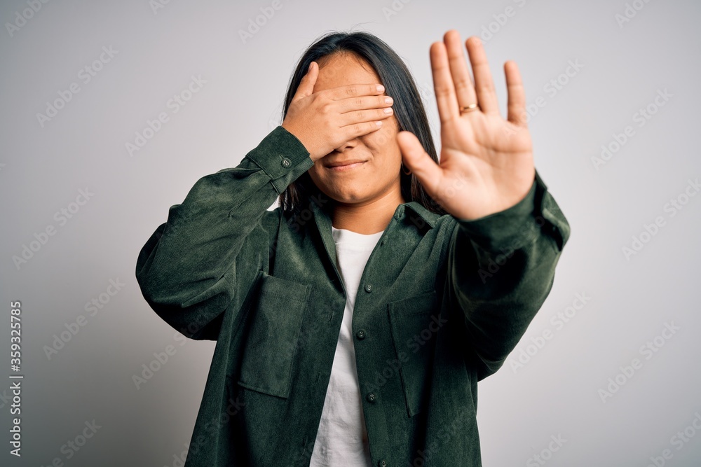 Young beautiful asian woman wearing casual shirt standing over isolated white background covering eyes with hands and doing stop gesture with sad and fear expression. Embarrassed and negative concept. Young beautiful asian woman wearing casual shirt standing over isolated white background covering eyes with hands and doing stop gesture with sad and fear expression. Embarrassed and negative concept.