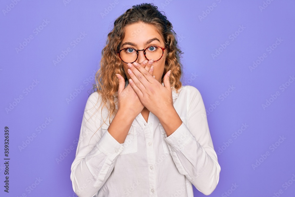 Young beautiful woman with blue eyes wearing casual shirt and glasses over purple background shocked covering mouth with hands for mistake. Secret concept. Young beautiful woman with blue eyes wearing casual shirt and glasses over purple background shocked covering mouth with hands for mistake. Secret concept.