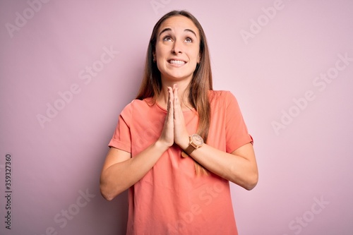 Young beautiful woman wearing casual t-shirt standing over isolated pink background begging and praying with hands together with hope expression on face very emotional and worried. Begging. © Krakenimages.com