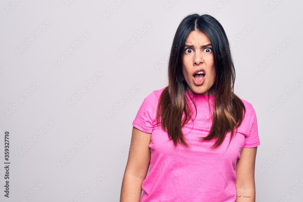 Young beautiful brunette woman wearing casual pink t-shirt standing over white background In shock face, looking skeptical and sarcastic, surprised with open mouth Young beautiful brunette woman wearing casual pink t-shirt standing over white background In shock face, looking skeptical and sarcastic, surprised with open mouth