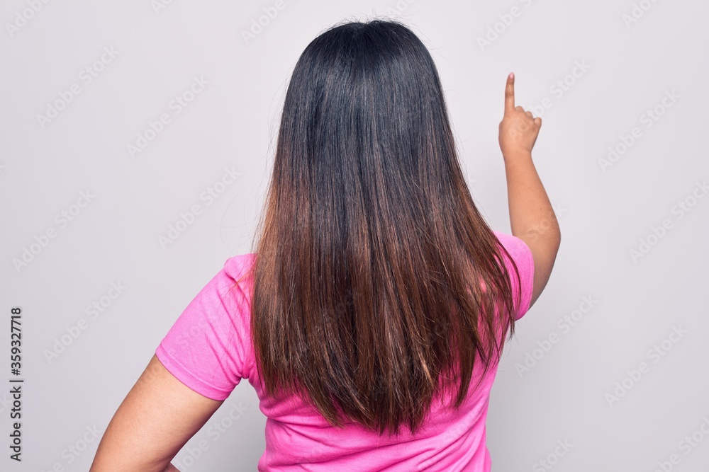 Young beautiful brunette woman wearing casual pink t-shirt standing over white background Posing backwards pointing ahead with finger hand Young beautiful brunette woman wearing casual pink t-shirt standing over white background Posing backwards pointing ahead with finger hand