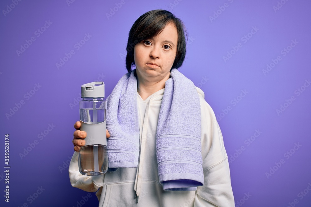 Young down syndrome fitness woman training at gym holding water bottle and sport towel with a confident expression on smart face thinking serious Young down syndrome fitness woman training at gym holding water bottle and sport towel with a confident expression on smart face thinking serious