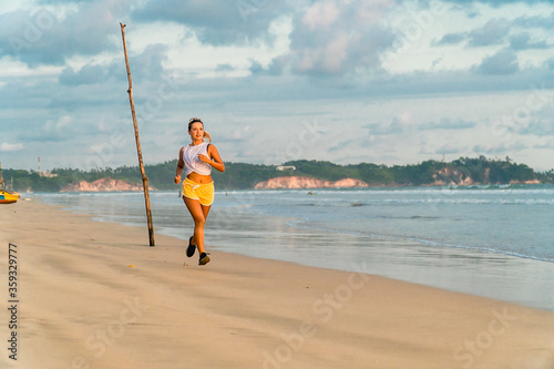 Fit young woman jogging on the beach. Sea shore running workout outdoor. Bright sports wear, positive active lifestyle