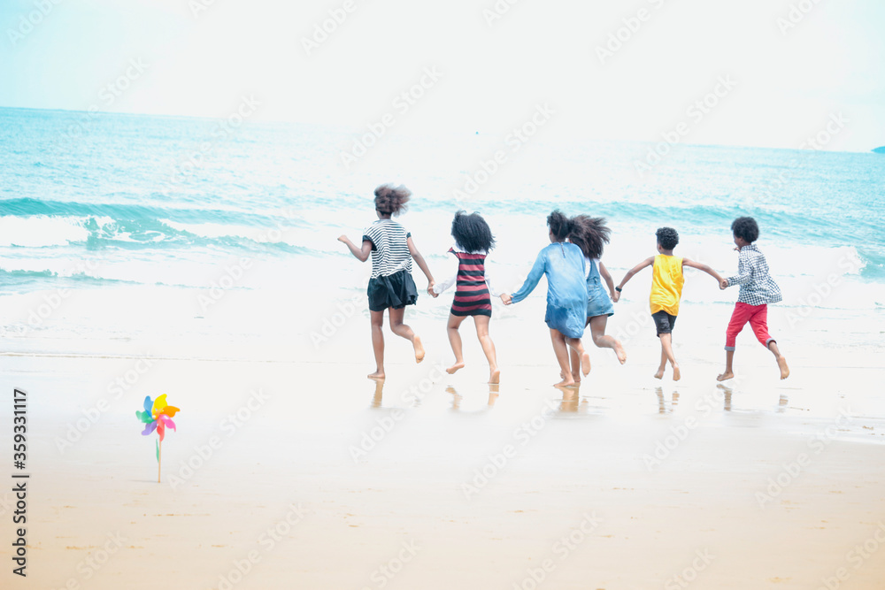 Group of six boys and girls holding hands in a line running to sea water, cute kids having fun on sandy summer beach, happy childhood friend playing on tropical sea