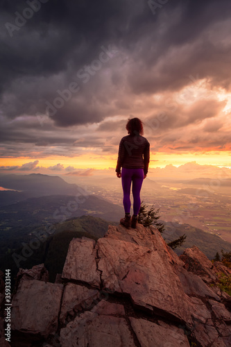 Adventurous Girl on top of a Rocky Mountain overlooking the beautiful Canadian Nature Landscape during a dramatic Sunset. Taken in Chilliwack  East of Vancouver  British Columbia  Canada.