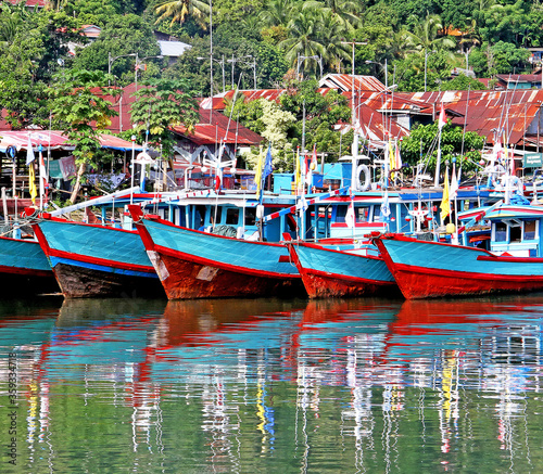 Colorful blue and red fishing boats in the Batang Arau river and port in Padang City in West Sumatra, Indonesia. © LilyRosePhotos