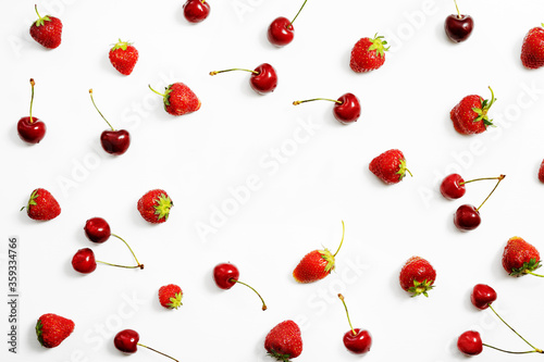 Berries of ripe strawberries and cherries are scattered on a white table with copy space. Top view.