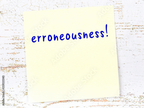 Yellow sticky note on wooden wall with handwritten word erroneousness photo