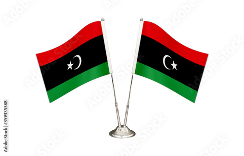 Free Download Libya table flag isolated on white ground. Two flag poles with flags and Libya flag on the table. - GFXLoad