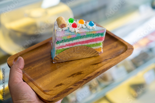 Piece of Rainbow Cake on wooden plate in shop