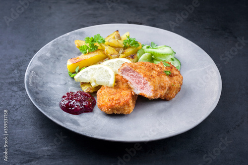 Traditional deep fried veal steak with fried potatoes and cucumber salad offered as closeup on a modern design plate with copy space