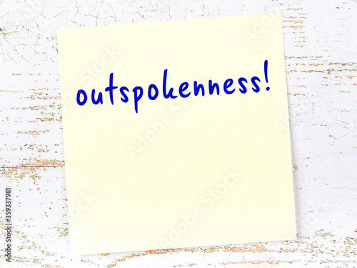 Yellow sticky note on wooden wall with handwritten word outspokenness photo