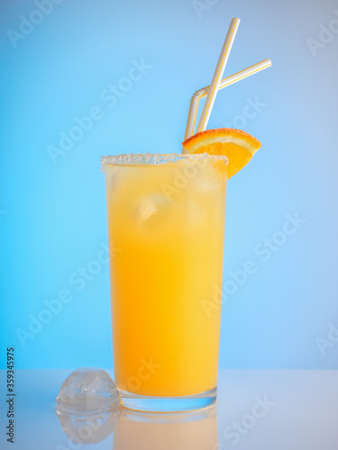 glass of ice orange juice with straw on blue background