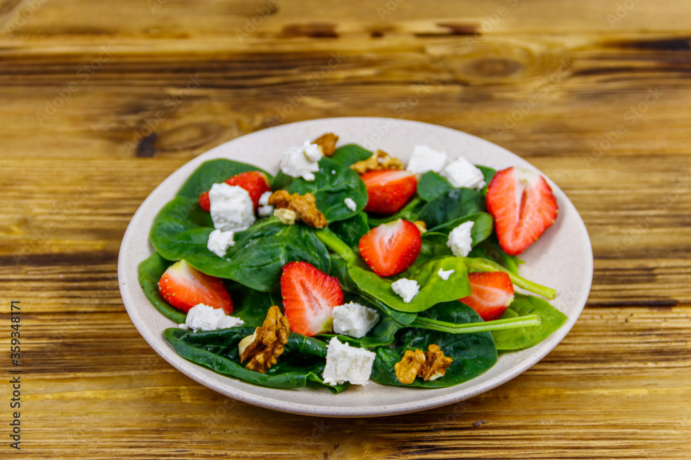 Fresh healthy salad with strawberry, spinach, walnuts and feta cheese on wooden table