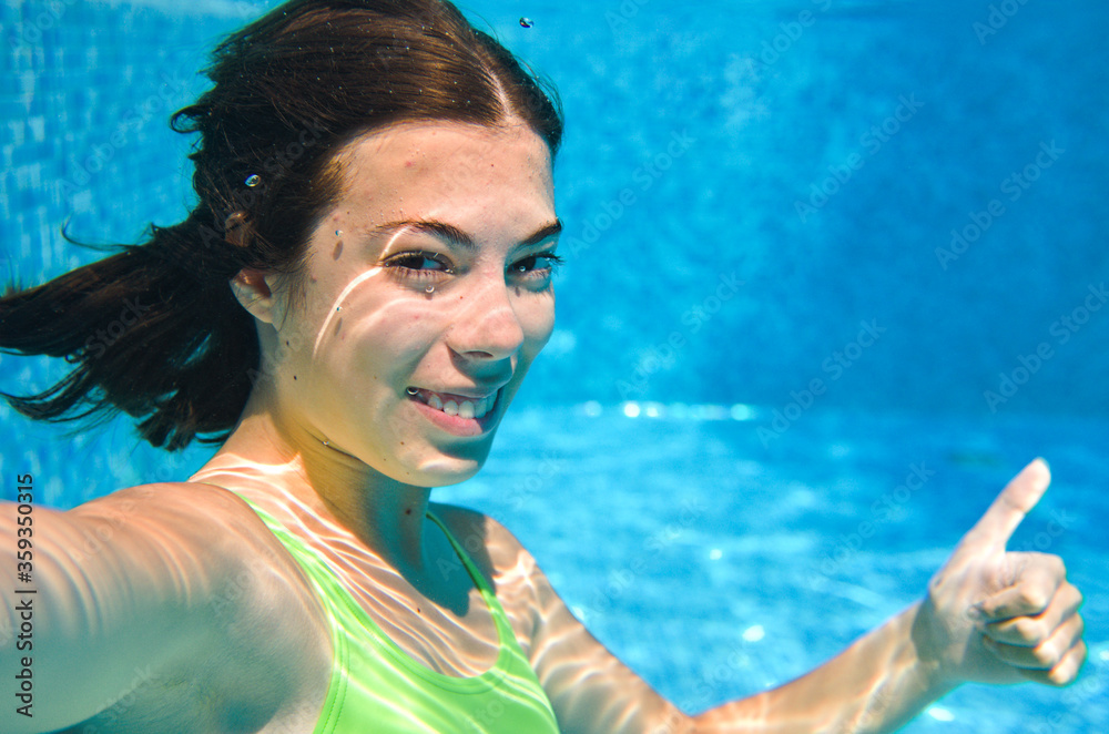 Child swims underwater in swimming pool, happy active teenager girl dives and has fun under water, kid fitness and sport on family vacation on resort
