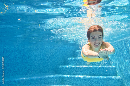 Child swims underwater in swimming pool, happy active teenager girl dives and has fun under water, kid fitness and sport on family vacation on resort 