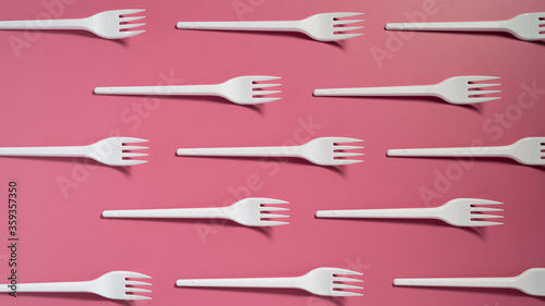 Many plastic forks on a pink background. Top view