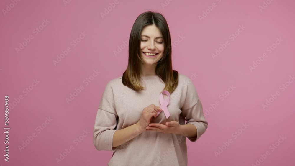 Kind brunette woman holding pink ribbon, symbol of breast cancer awareness, recommendation and warning of cancer prevention, female health diagnostics. indoor studio shot isolated on pink background Kind brunette woman holding pink ribbon, symbol of breast cancer awareness, recommendation and warning of cancer prevention, female health diagnostics. indoor studio shot isolated on pink background