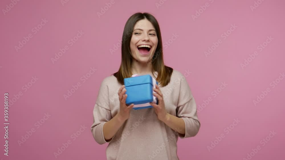 Happy birthday! Charming young woman expressing great joy and surprise when receiving present, shaking gift box, listening with interest what's inside. indoor studio shot isolated on pink background Happy birthday! Charming young woman expressing great joy and surprise when receiving present, shaking gift box, listening with interest what's inside. indoor studio shot isolated on pink background
