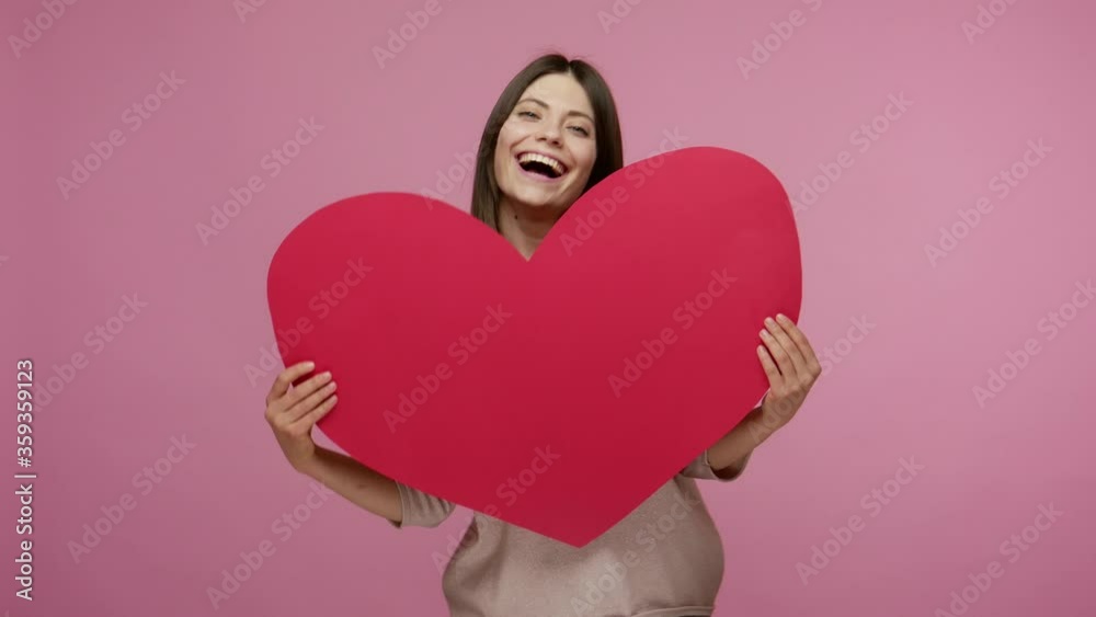 Cheerful brunette girl full of love and energy holding huge heart, laughing at camera, dancing and expressing romantic feelings, care and generosity. indoor studio shot isolated on pink background Cheerful brunette girl full of love and energy holding huge heart, laughing at camera, dancing and expressing romantic feelings, care and generosity. indoor studio shot isolated on pink background