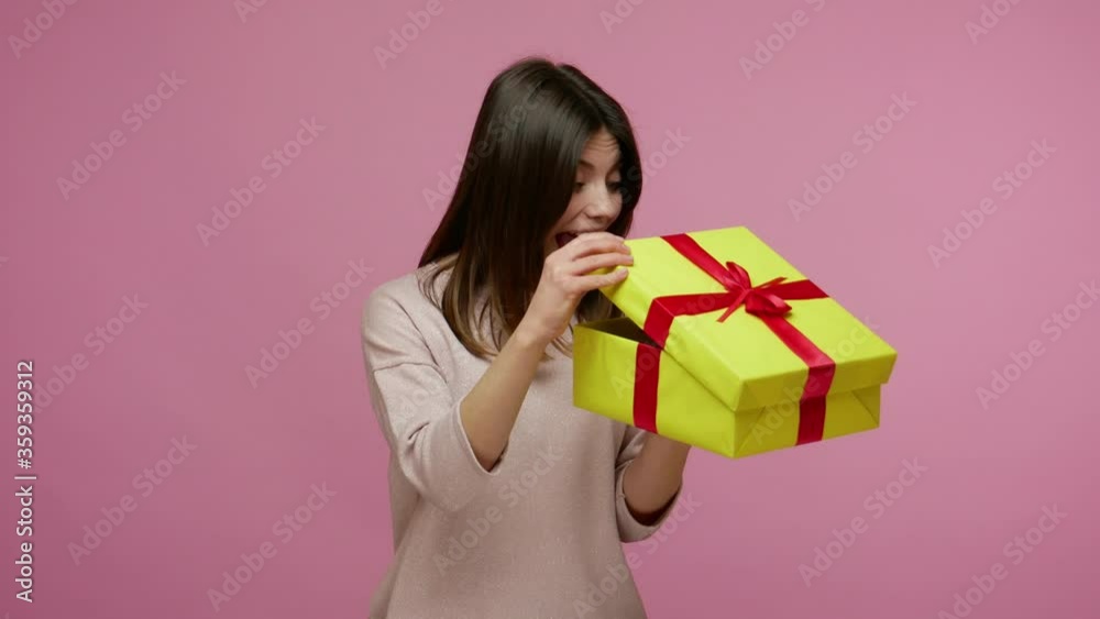 Beautiful cheerful brunette woman opening gift box and smiling joyfully, looking amazed satisfied with nice present, unexpected birthday surprise. indoor studio shot isolated on pink background Beautiful cheerful brunette woman opening gift box and smiling joyfully, looking amazed satisfied with nice present, unexpected birthday surprise. indoor studio shot isolated on pink background