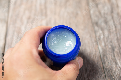 Принти на полотні A view of a hand holding a jar of cough suppressant ointment against a wood table surface