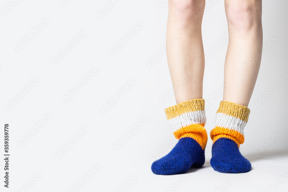 Female legs in warm multi-colored socks on a light background