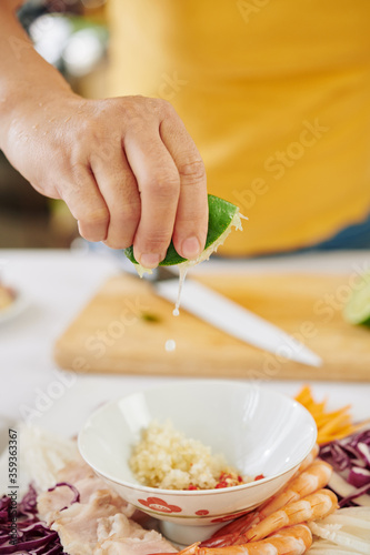 Close-up image of woman squeezing half of fresh lime into bowl with diced garlic and paprika