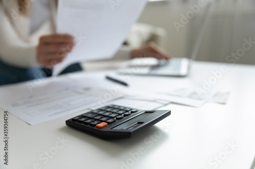 Close up view on coffee table lie calculator papers documents unrecognizable woman working on laptop indoor. Small business owner do analyze income and expenses, pay bills use internet banking concept