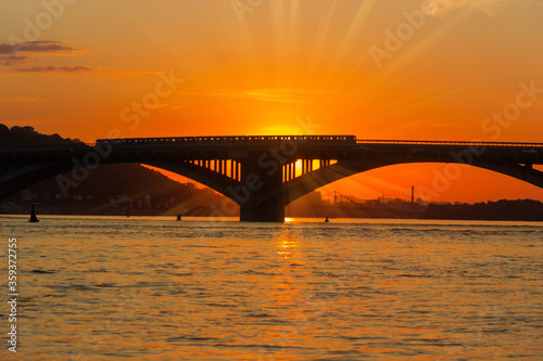 Fototapeta Naklejka Na Ścianę i Meble -  Silhouette of bridge across river at sunset in backlight
