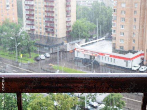 wet balcony railing and above view of blurred street on background in heavy rain in Moscow city (focus on the railing)