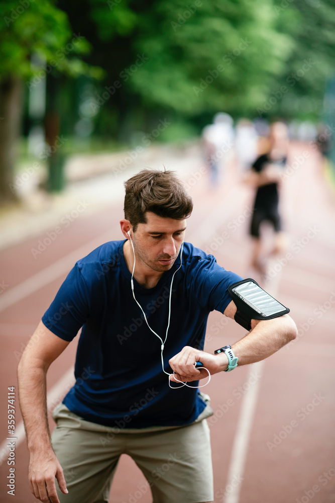 Fototapeta premium Young man checking his heart rate during work out. Young man exercising on athletics track