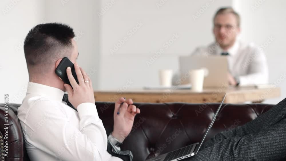 man boss sitting on sofa and negotiating on phone. business call. talking to colleague coworker and discussing project deadline. concept laptop, conversation. in white office workplace background man boss sitting on sofa and negotiating on phone. business call. talking to colleague coworker and discussing project deadline. concept laptop, conversation. in white office workplace background