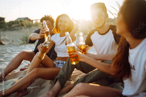 Young people sitting together at beach, drinking beer and having a party. Group of friends cheers with beers at the beach during summer vacation. © maxbelchenko