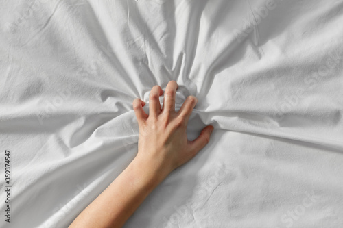 bedtime, sex and rest concept - hand of woman squeezing white bed sheet