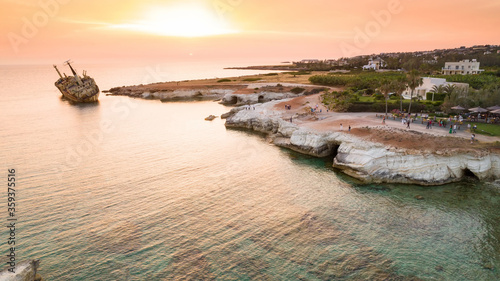 Aerial bird’s eye view of the abandoned ship wreck EDRO III in Pegeia, Paphos, Cyprus from above at sunset. Rusty shipwreck stranded on Peyia rocks at sea caves, Coral Bay in Pafos, standing on coast.