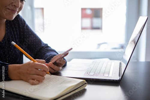 young woman writing in notebook, while watching a webinar on the laptop.