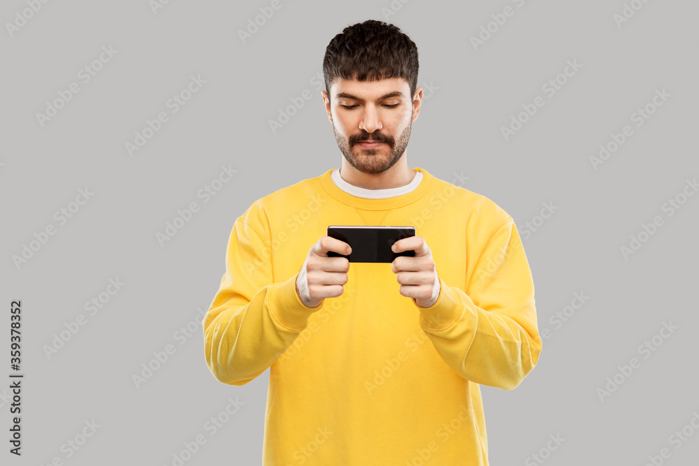 technology, communication and people concept - young man playing game on smartphone over grey background technology, communication and people concept - young man playing game on smartphone over grey background