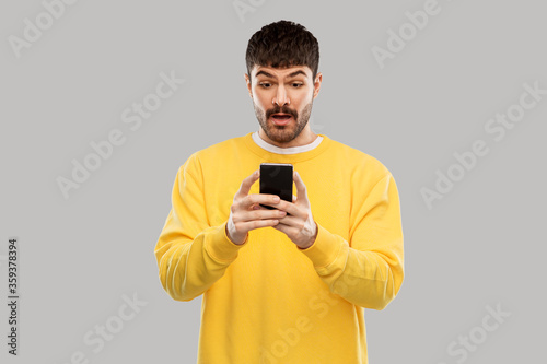 technology, communication and people concept - surprised young man with smartphone over grey background © Syda Productions
