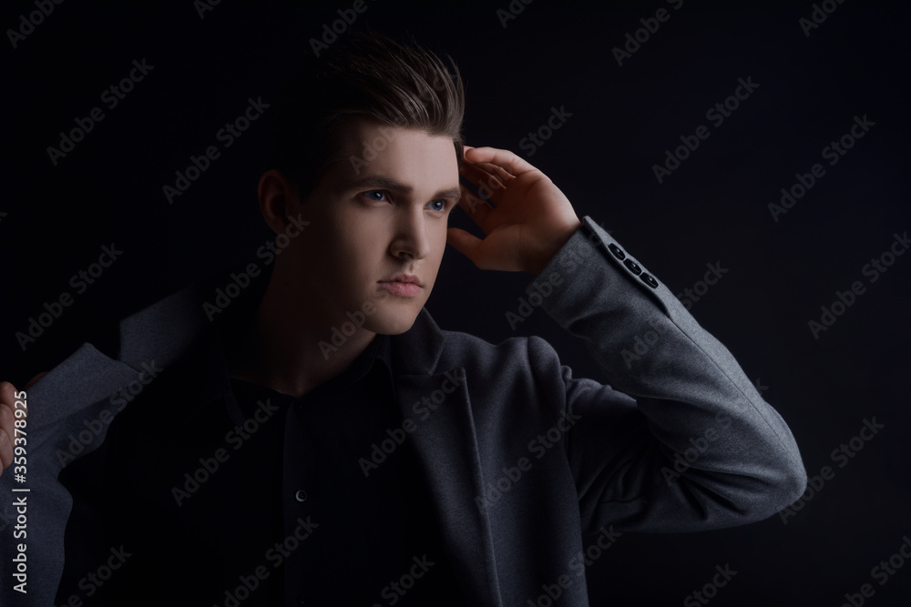 Studio portrait of a man with a raincoat on a black background. Muddy with a perfect hairstyle, European appearance posing, model in the side light. Personal care Studio portrait of a man with a raincoat on a black background. Muddy with a perfect hairstyle, European appearance posing, model in the side light. Personal care
