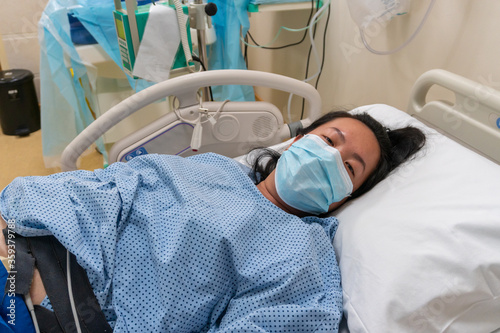 Young Asian Chinese lady in Contraction pain on hospital labour room ward bed waiting to delivery newborn baby